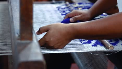 closeup of hands weaving warp loom through weaving frame, white and deep indigo blue cotton fabric yarns
