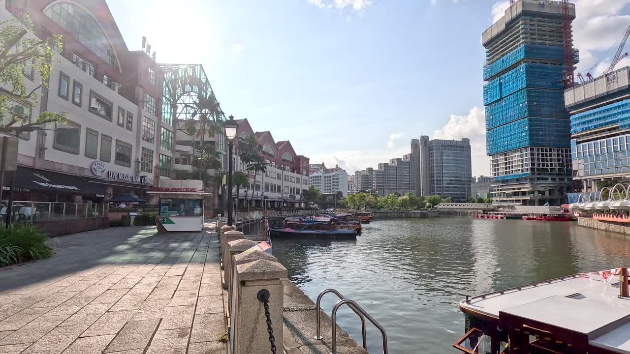 Daytime boat glides along Singapore riverfront, passing colorful Clarke Quay buildings and construction skyline