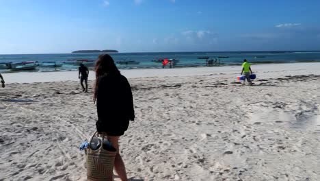 woman walking towards the boats at the shore with a bag and looking back over her shoulder