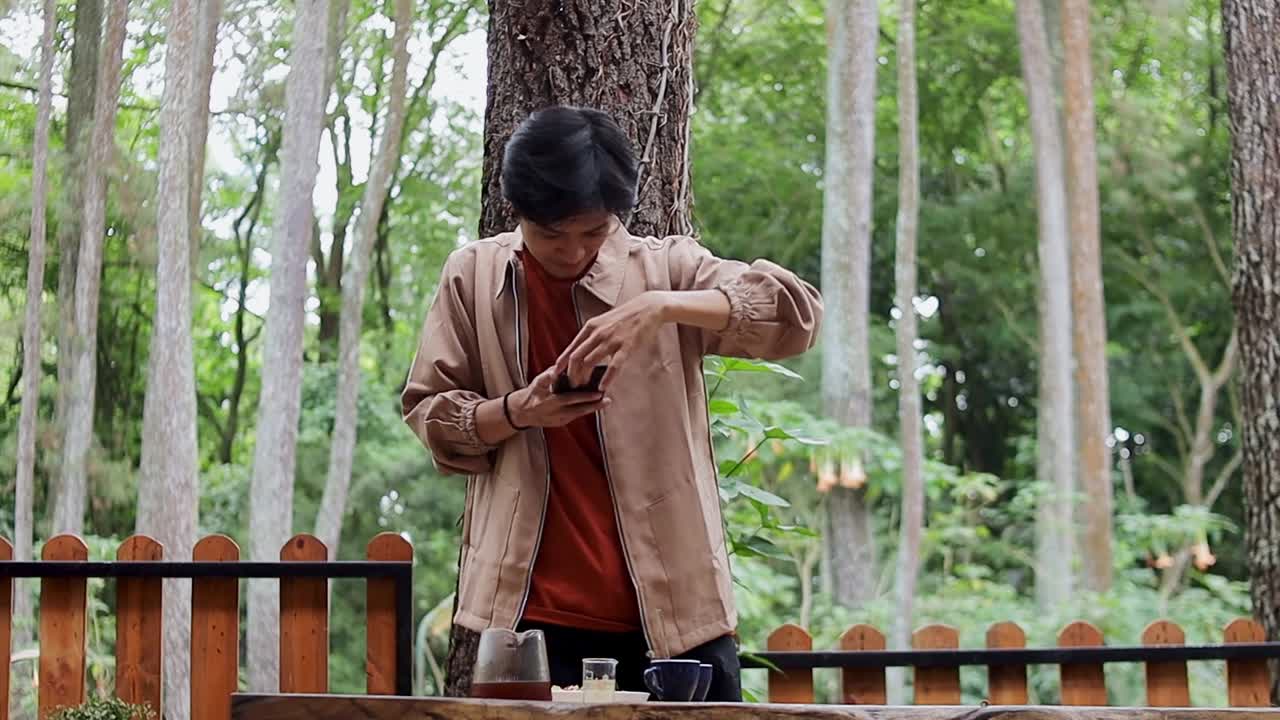 Confident Young asian man captures drink moment with smartphone at outdoor cafe