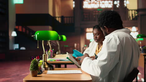 estudiantes de medicina negros comparando conocimientos y notas de clase en la biblioteca