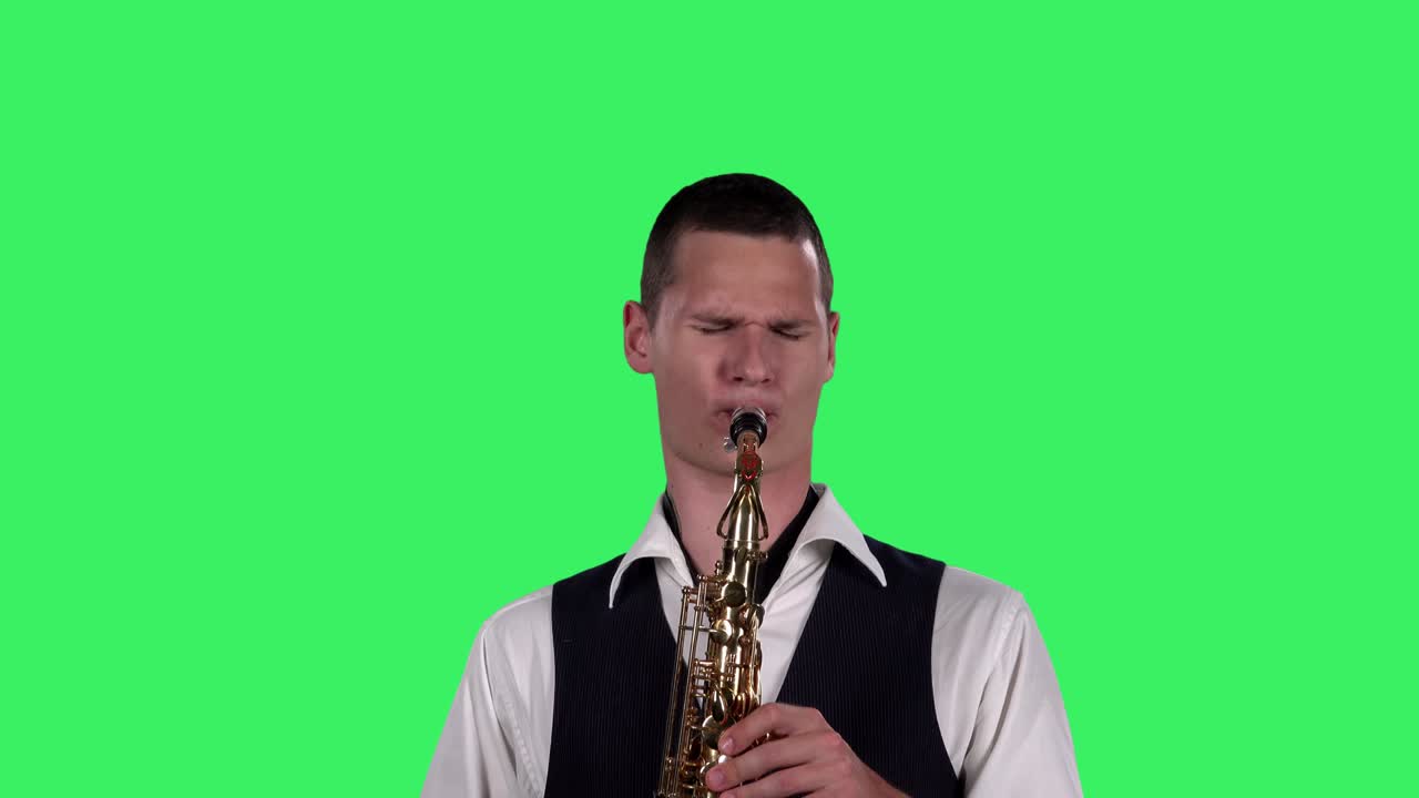 초상화: 스타일리시한 젊은이가 스튜디오에서 녹색 스크린에서 색소폰으로 빠른 멜로디를 연주합니다. 색소폰 연주자가 솔로를 연주하고 있습니다.