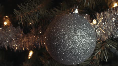 silver glitter christmas tree ornament with white dots hanging on the tree, pan shoot