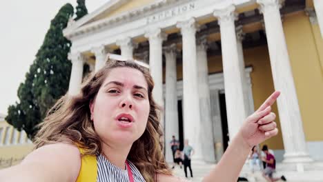 young woman pointing at zappeion hall while vlogging in athens