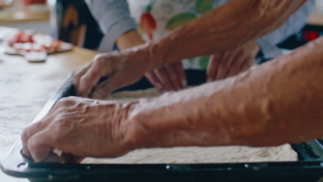 hands of elderly woman and her granddaughter spreading dough in baking tray