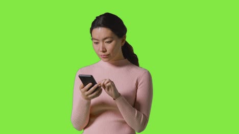 studio shot of woman scrolling through messages or content on mobile phone in front of green screen