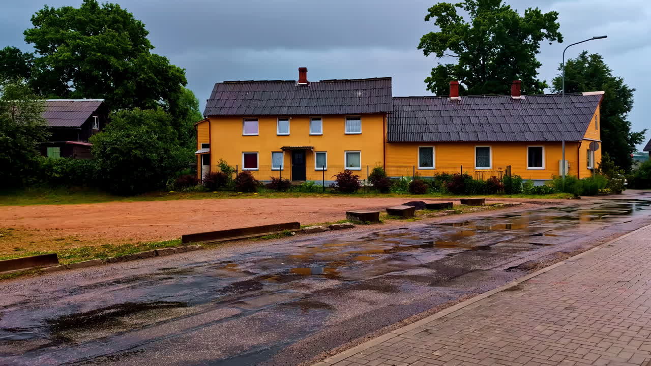Yellow wooden house in Latvia with puddles and wet street after summer rain