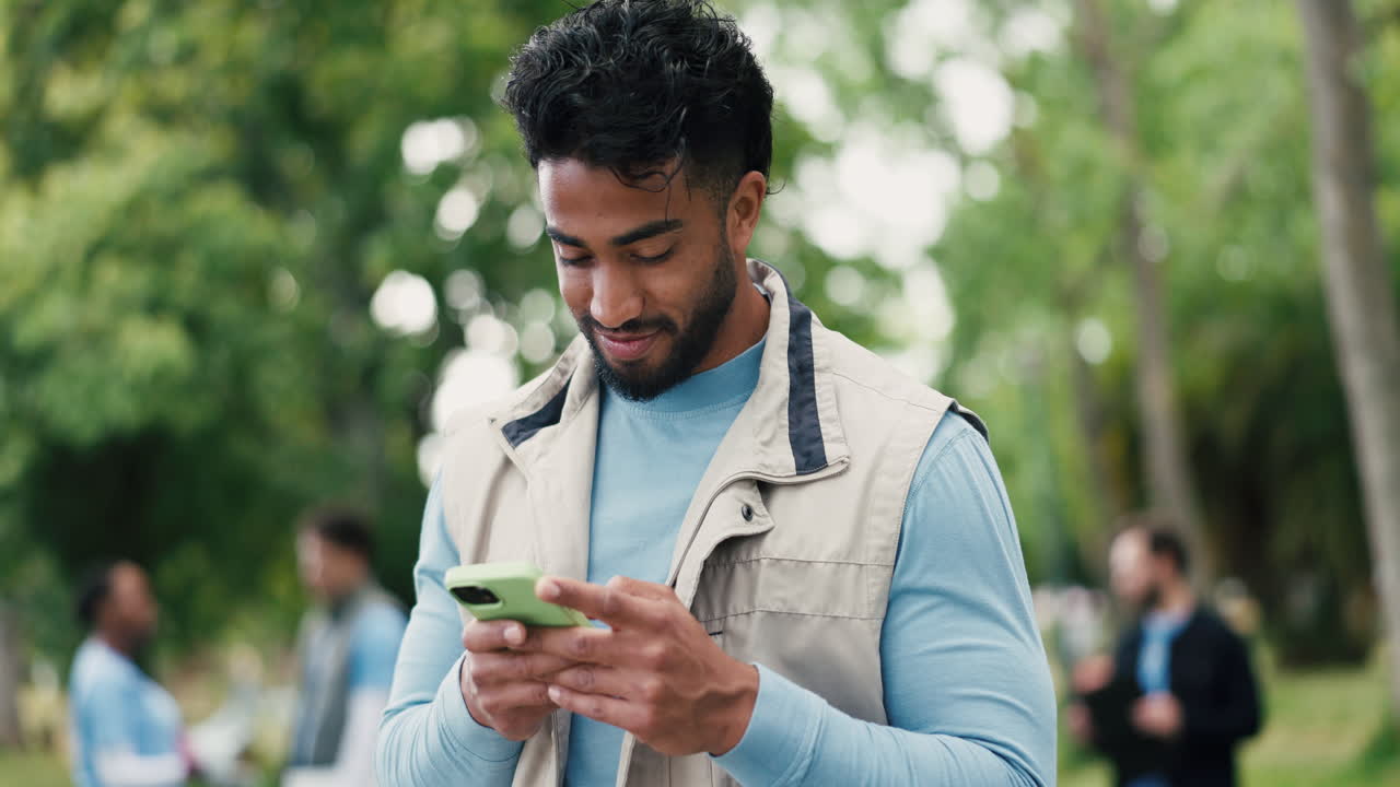 Giovane uomo sorridente che messaggia con lo smartphone al parco
