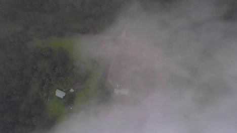 Aerial-shot-flying-through-the-clouds-revealing-the-lush-green-fields-of-Berry,-NSW-Australia-below