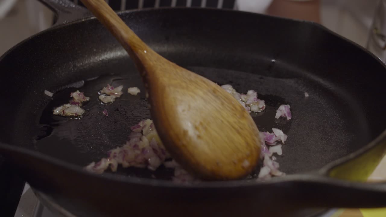 Stirring onion on hot frying pan with wooden spoon