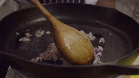 stirring onion on hot frying pan with wooden spoon