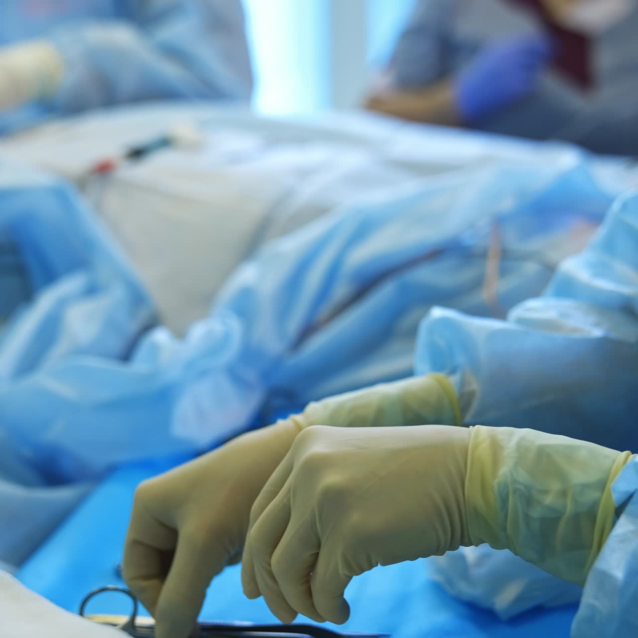Diverse metal tools on the little table. Medic comes up to the table picking up some instruments from doctors. Surgery in progress at backdrop