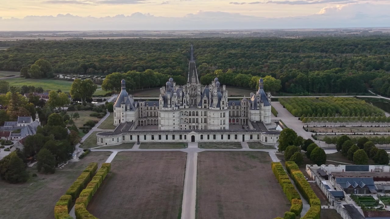 Riprese aeree del Castello di Chambord e dei suoi giardini formali, con la facciata simmetrica, la guglia centrale, i terreni curati e la foresta circostante visibili al tramonto