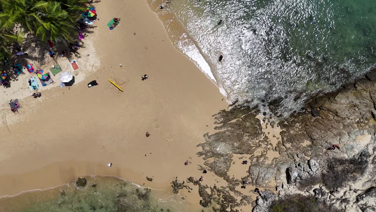 las imágenes de drones capturan una vibrante playa en phuket, tailandia, mostrando bañistas de sol, paraguas y costas rocosas a la luz del día.