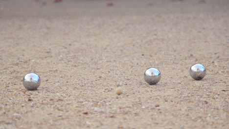 slow-motion close-up of pétanque balls. one ball hits another, knocking it away from the cochonnet. dust rises, capturing the precision of the strike in daylight.