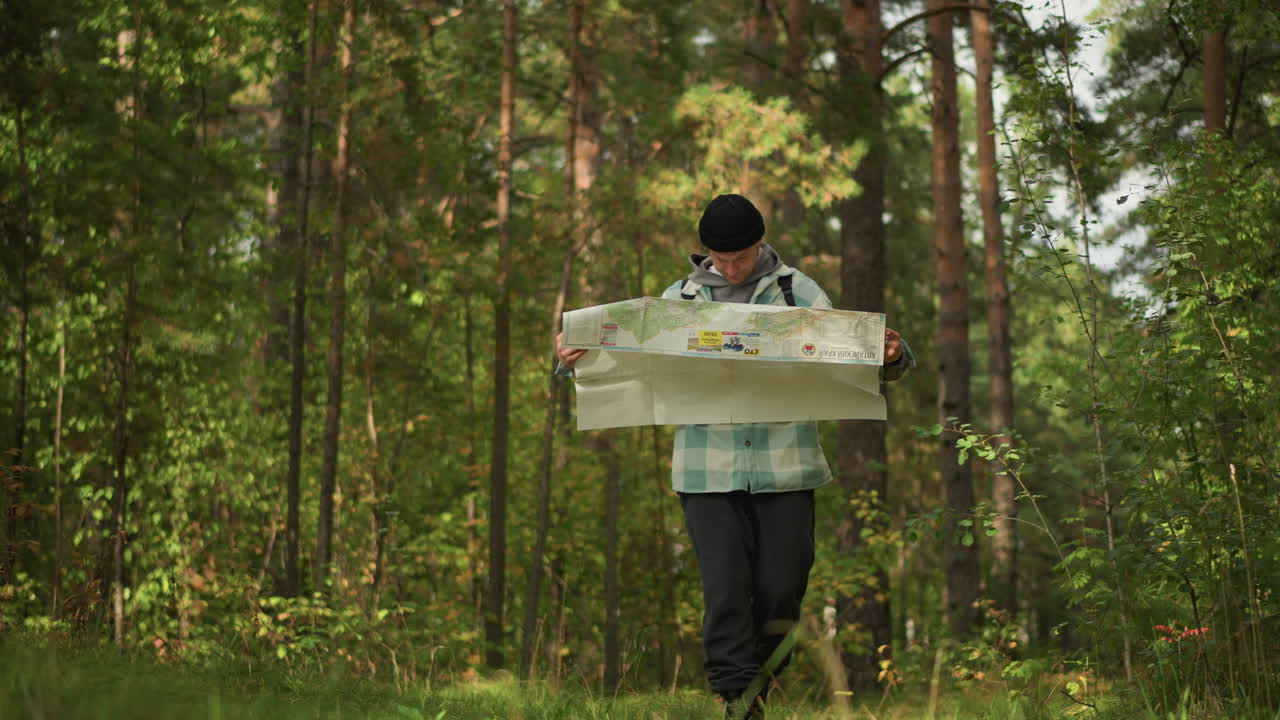 white male hiker studying unfolded map in pine forest, inspecting scale and compass, planning route with intent, sunlit clearing and attentive posture signal focused off grid navigation
