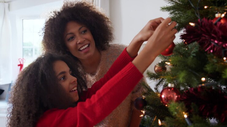 Mother And Daughter Hanging Decorations On Christmas Tree At Home