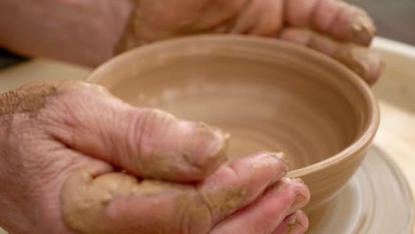 hands shaping a clay bowl on a pottery wheel