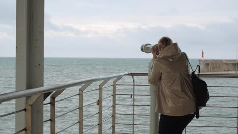 Frau-Blickt-Am-Aussichtspunkt-Durch-Ein-Fernglas-Auf-Das-Meer