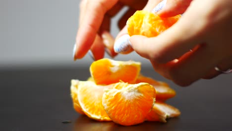 las manos de la mujer en un hermoso esmalte de uñas dividen la mandarina en rebanadas con un fondo borroso