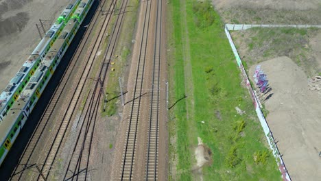 scenic aerial shot of passenger train driving into sunset on train tracks surrounded by trees above cityscape forward