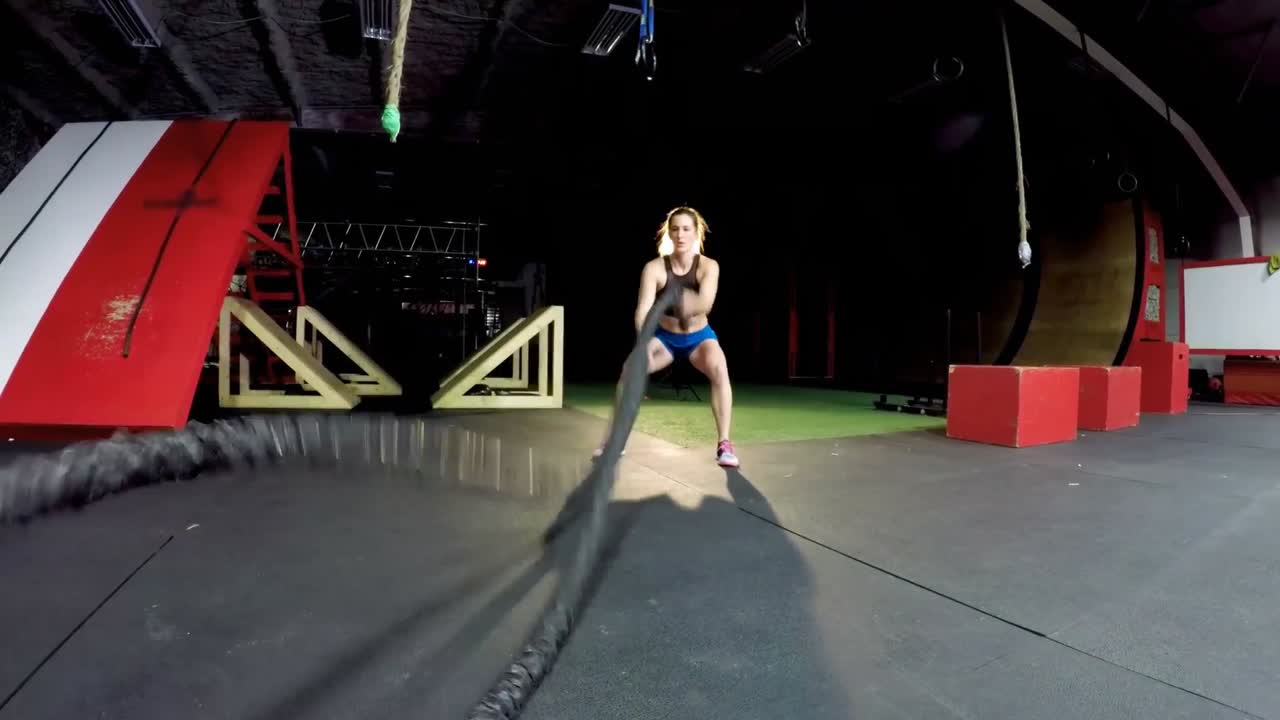 атлетическая женщина выполняет упражнения с боевой веревкой 4к