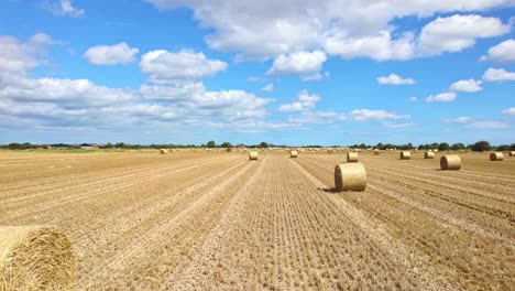 En-Una-Vista-Aérea,-Podemos-Ver-Turbinas-Eólicas-Girando-Con-Gracia-En-El-Campo-Recién-Cosechado-De-Un-Granjero-De-Lincolnshire,-Con-Balas-De-Heno-Doradas-Creando-Un-Primer-Plano-Pintoresco.