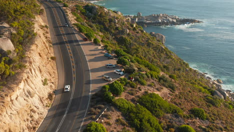 vehicles driving along victoria road with ocean views near oudekraal, south africa