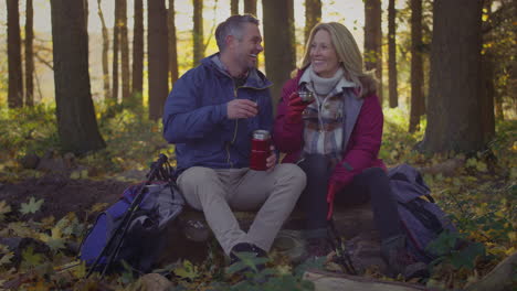 mature couple sitting on log stop for rest and hot drink on walk through fall or winter countryside - shot in slow motion