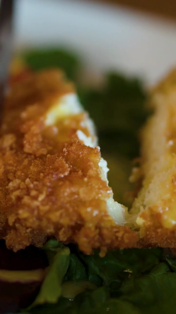 Extreme macro close up shows a knife slicing through golden brown breaded fried chicken breast