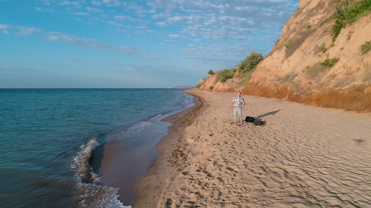 Sea shore and a singer man. Musician singing on a sand beach near the hills. Beautiful nature with blue sea water and coast. Motion camera forward.