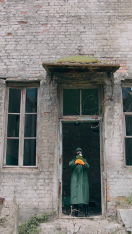 human in infected zone. ecologist in protective suit and gas mask coming out the abandoned building and holding flowers in hands. vertical video