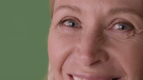 close up view of half face of blonde mature woman with blue eyes smiling at camera on green background