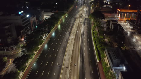 Niedrig-Fliegende-Luftkippwagenaufnahme-Einer-Leeren-Mehrspurigen-Straße-Im-Modernen-Stadtzentrum-Mit-Wolkenkratzern-Bei-Nacht