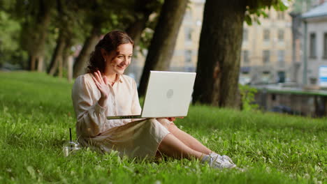Woman-making-video-laptop-webcam-conference-call-with-friends-or-family-sitting-on-grass-in-park