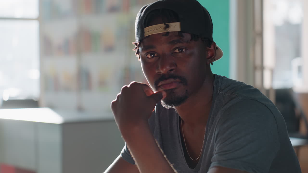 Reflective student sits in library with pen in hand, lifting head calmly from study session, lost in deep thought as sunlight filters through windows, creating serene atmosphere