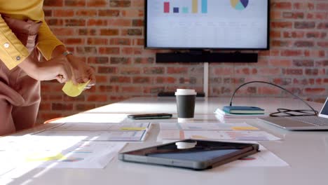 Midsection-of-african-american-casual-businesswoman-looking-at-documents-in-office,-slow-motion