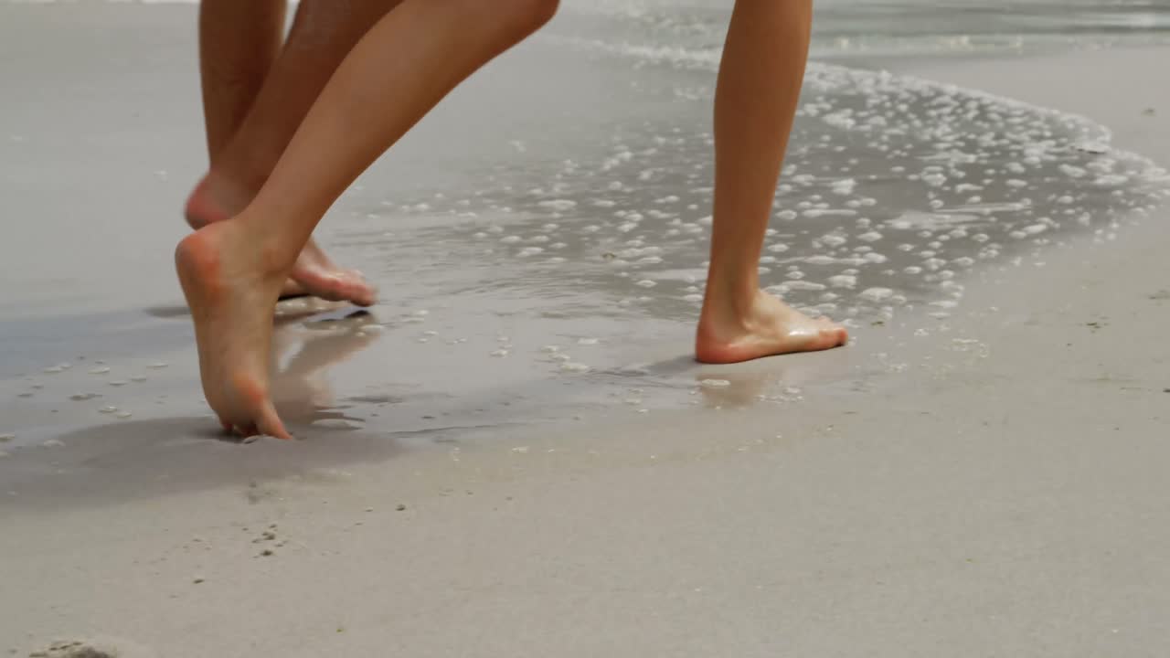 Sezione inferiore di una coppia che cammina scalza sulla spiaggia 4k