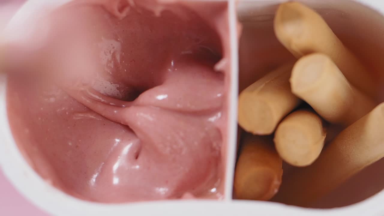 Intingere un bastoncino di biscotto in uno snack cremoso rosa