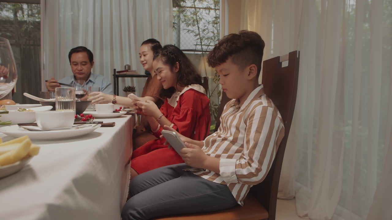 Boy and Girl Using Smartphones during Dinner with Family