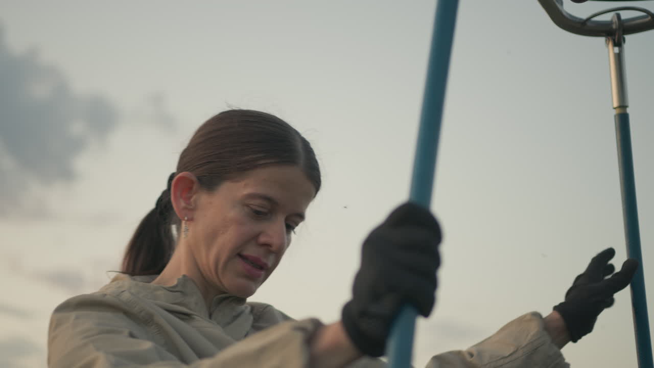 close up of woman in gloves detaching blue support rods from hot air balloon basket and burner assembly at dusk focused on hands and equipment removal against soft sky backdrop