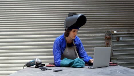 Female-welder-using-laptop-in-workshop-4k