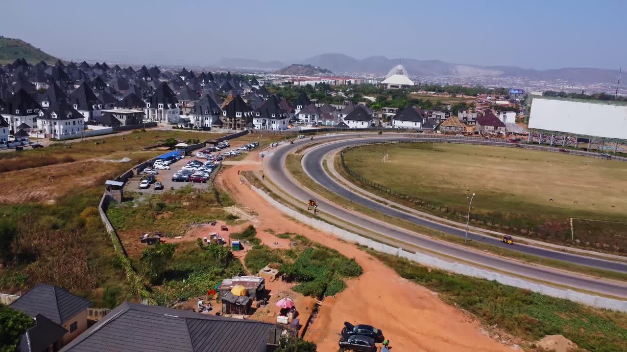Drone flyver over skure og en travl motorvej mod et smukt forstadskvarter i Abuja, Nigeria.