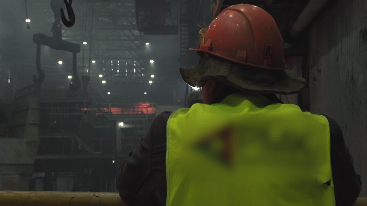 Lavoratore con Elmetto e Giubbotto di Sicurezza che Osserva Operazioni Industriali in Fabbrica