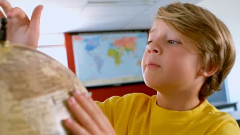 bonito escolar caucásico estudiando el globo en un aula en la escuela 4k