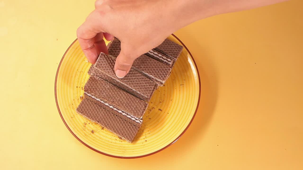 Mano che prende un biscotto wafer al cioccolato da un piatto giallo