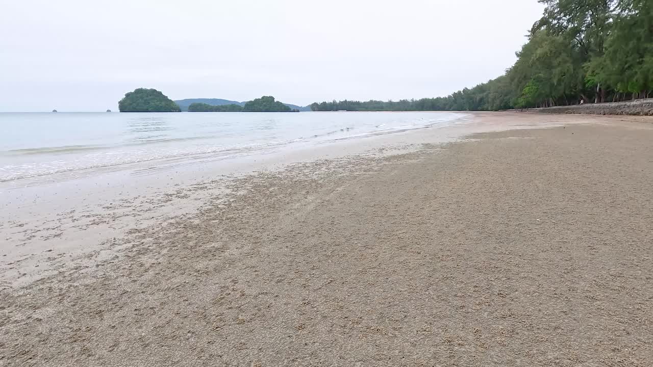 태국 크라비의 조용한 해변 장면, 부드러운 파도와 부드러운 자연 조명 아래 울창한 초록색을 보여줍니다.