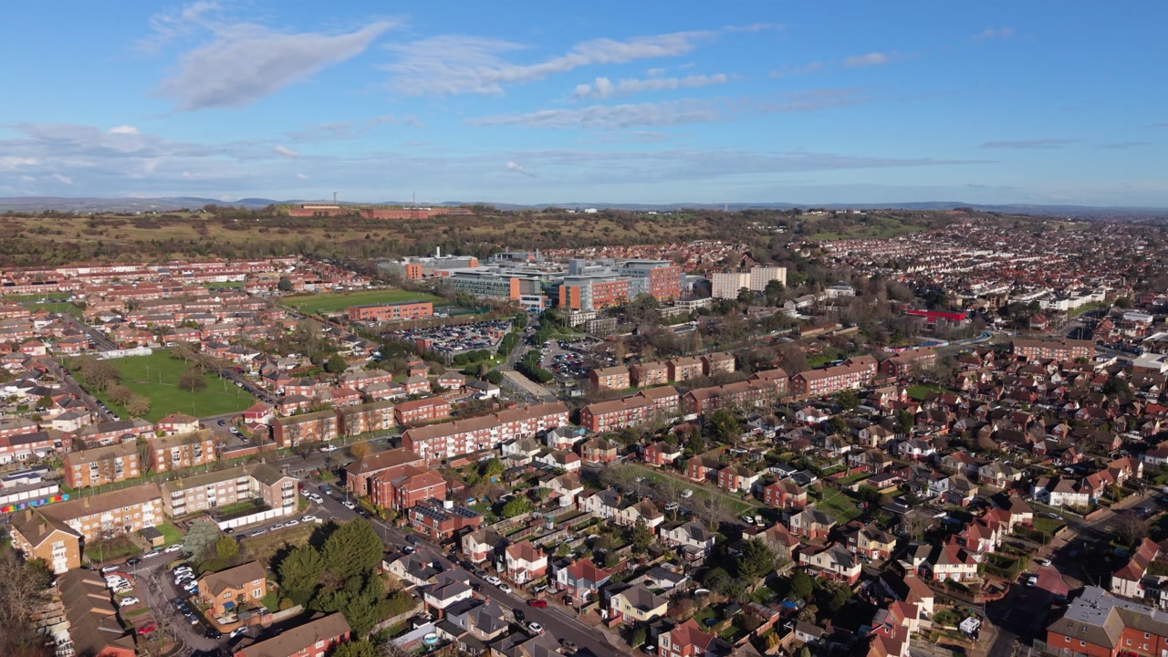 Portsmouth slow high drone flight directly towards Queen Alexandra Hospital with distant countryside views in bright afternoon sun flying over housing estates and green spaces