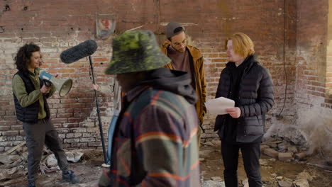 two production coworkers talking and reading a document about the movie in a ruined building the they looks at the camera