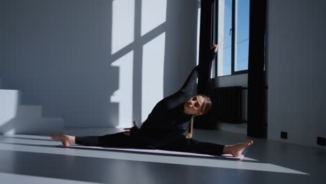 woman doing a yoga split on a mat in a studio